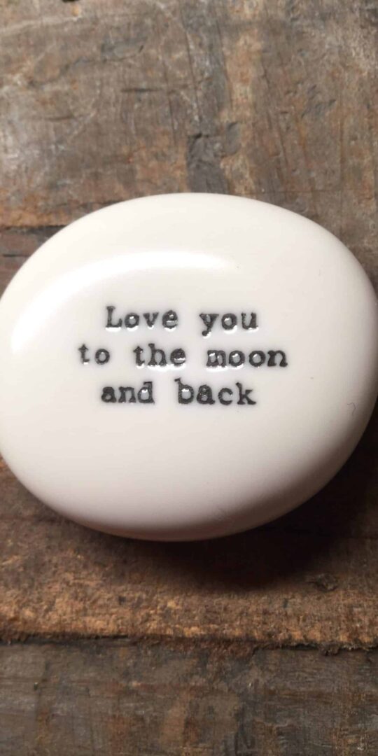 East Of India White Porcelain Pebble with Black Type Engraved. Saying: Love you To The Moon and Back.