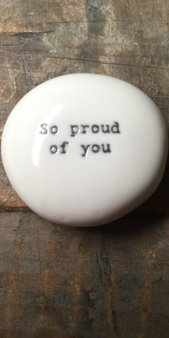 East Of India Small White Porcelain Pebble with Black Type Engraved. Saying: So Proud Of You