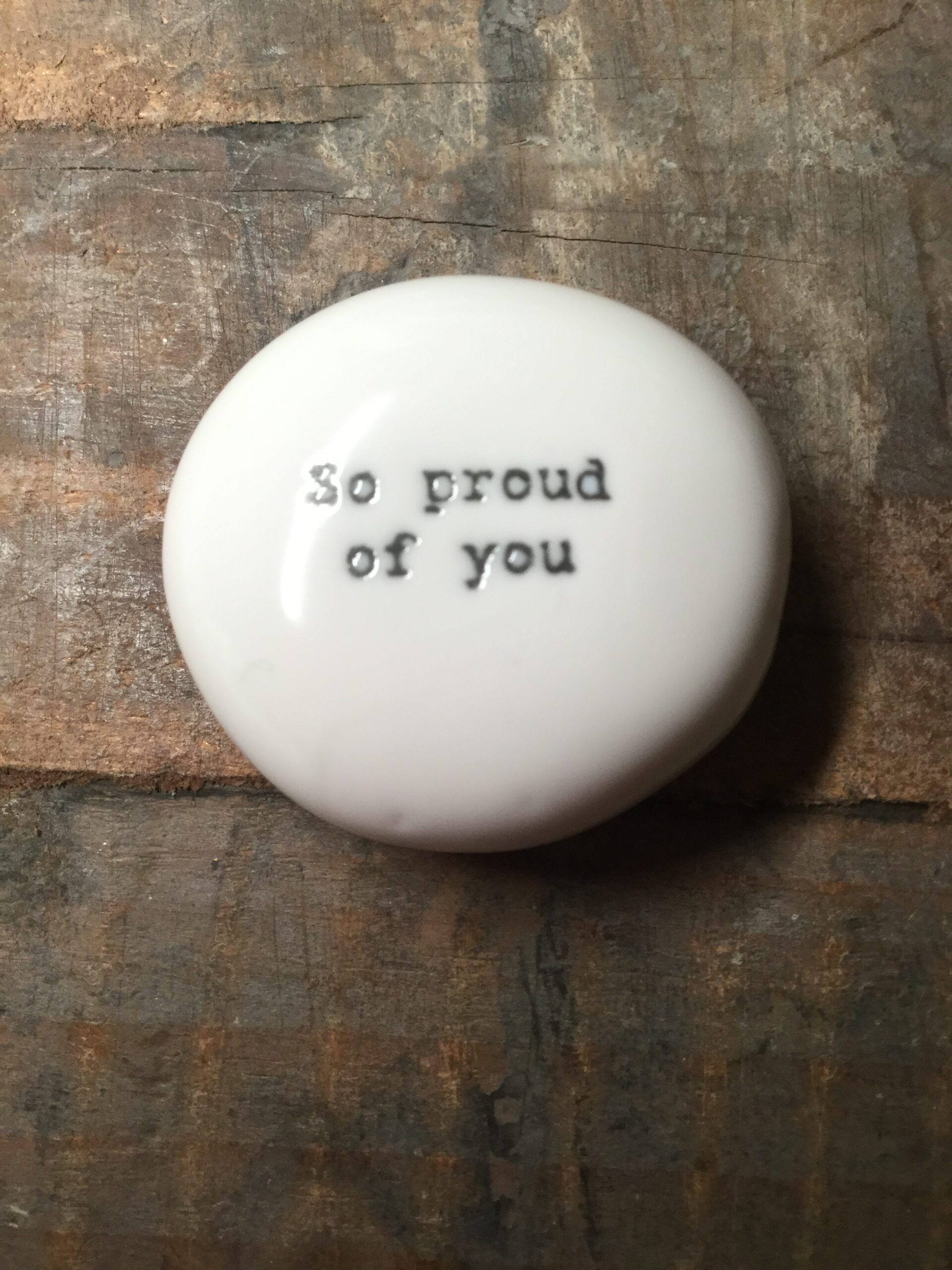 East Of India Small White Porcelain Pebble with Black Type Engraved. Saying: So Proud Of You